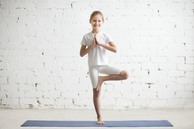 Girl child in Vrksasana pose, white studio background